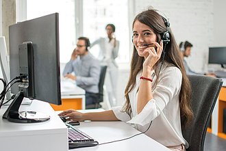 Eine Frau sitzt mit einem Headset am Computer.